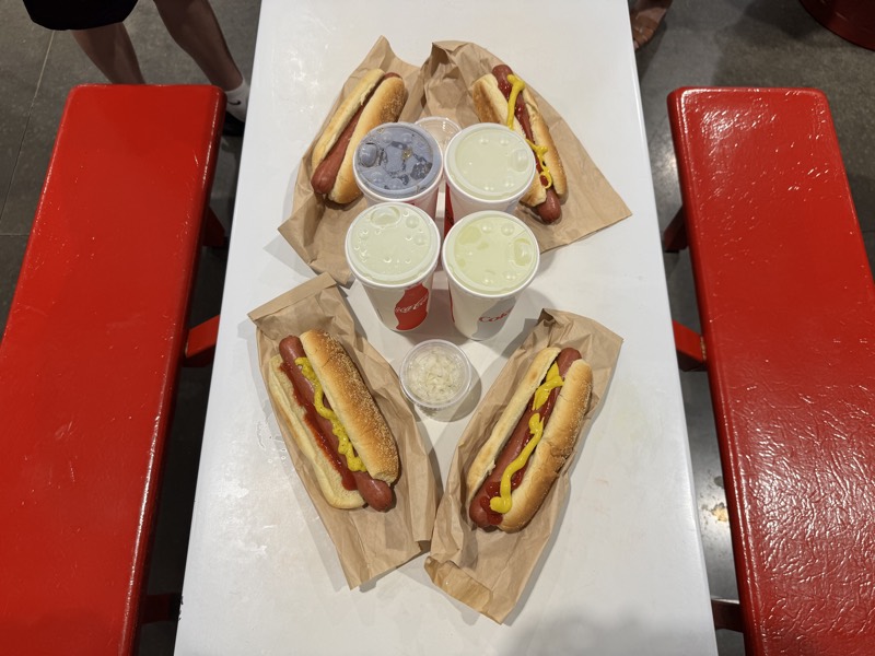 Four hot dogs and four sodas on a food court table. Six dollars, before tax.